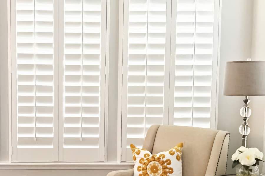 An armchair next to white Polywood interior shutters on a living room window