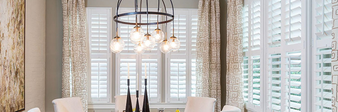Polywood shutters with patterned curtains in a dining room.